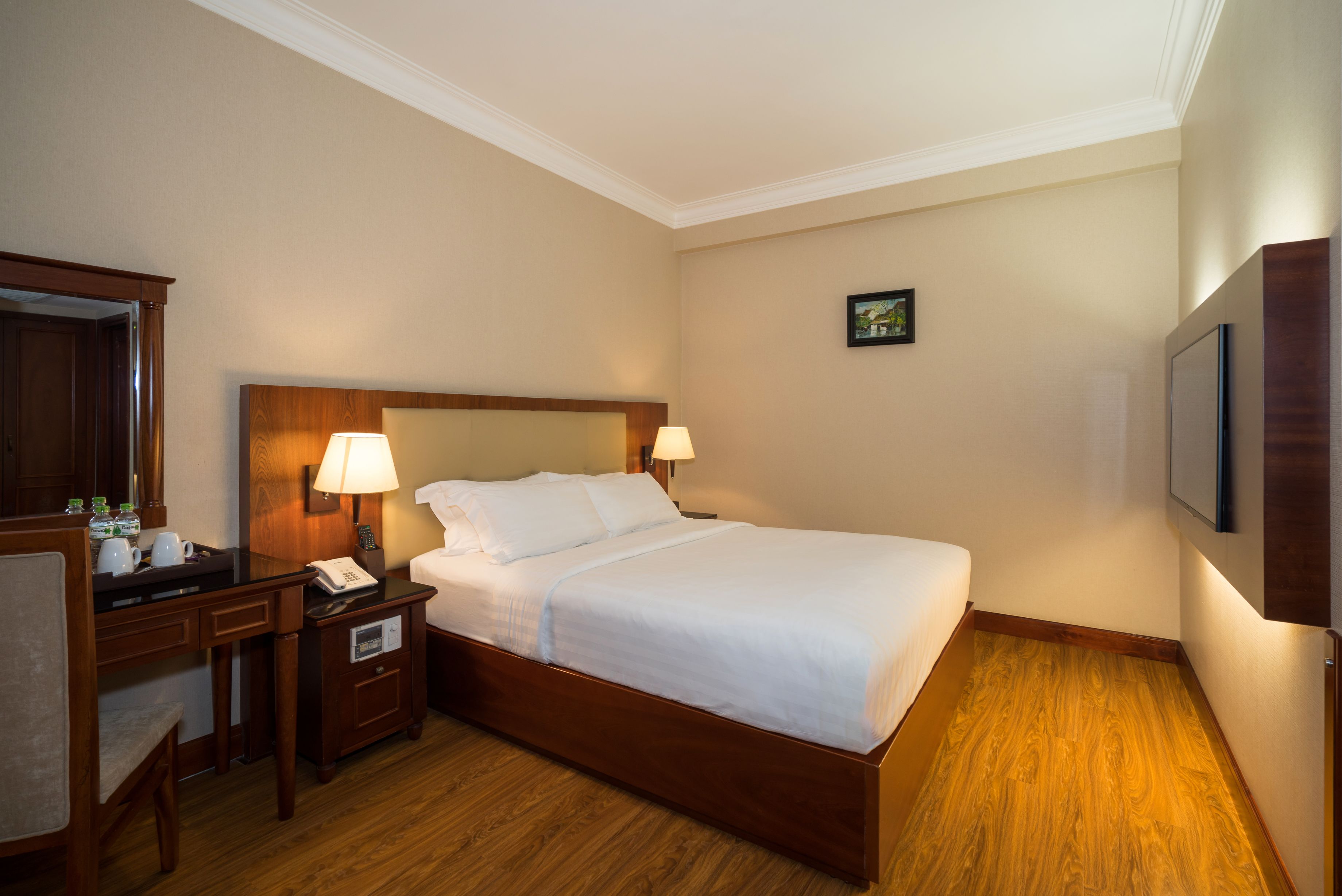 A hotel room with a wooden bed, two bedside tables with lamps, a desk with a telephone, and a small picture on the wall.