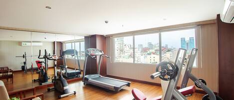 Un gimnasio espacioso con varios equipos de ejercicio, amplias ventanas con vista a la ciudad y suelo de madera.