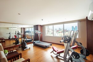 A spacious gym with various exercise equipment, large windows offering a city view, and a wooden floor.