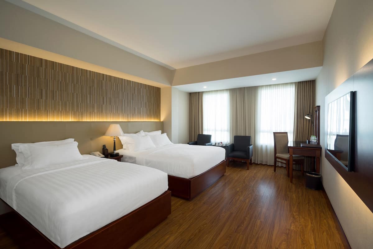 A hotel room with two beds, a desk, a chair, a TV, and a large window with curtains.