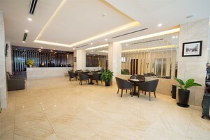 A hotel lobby with a reception desk, seating area, and a large potted plant.