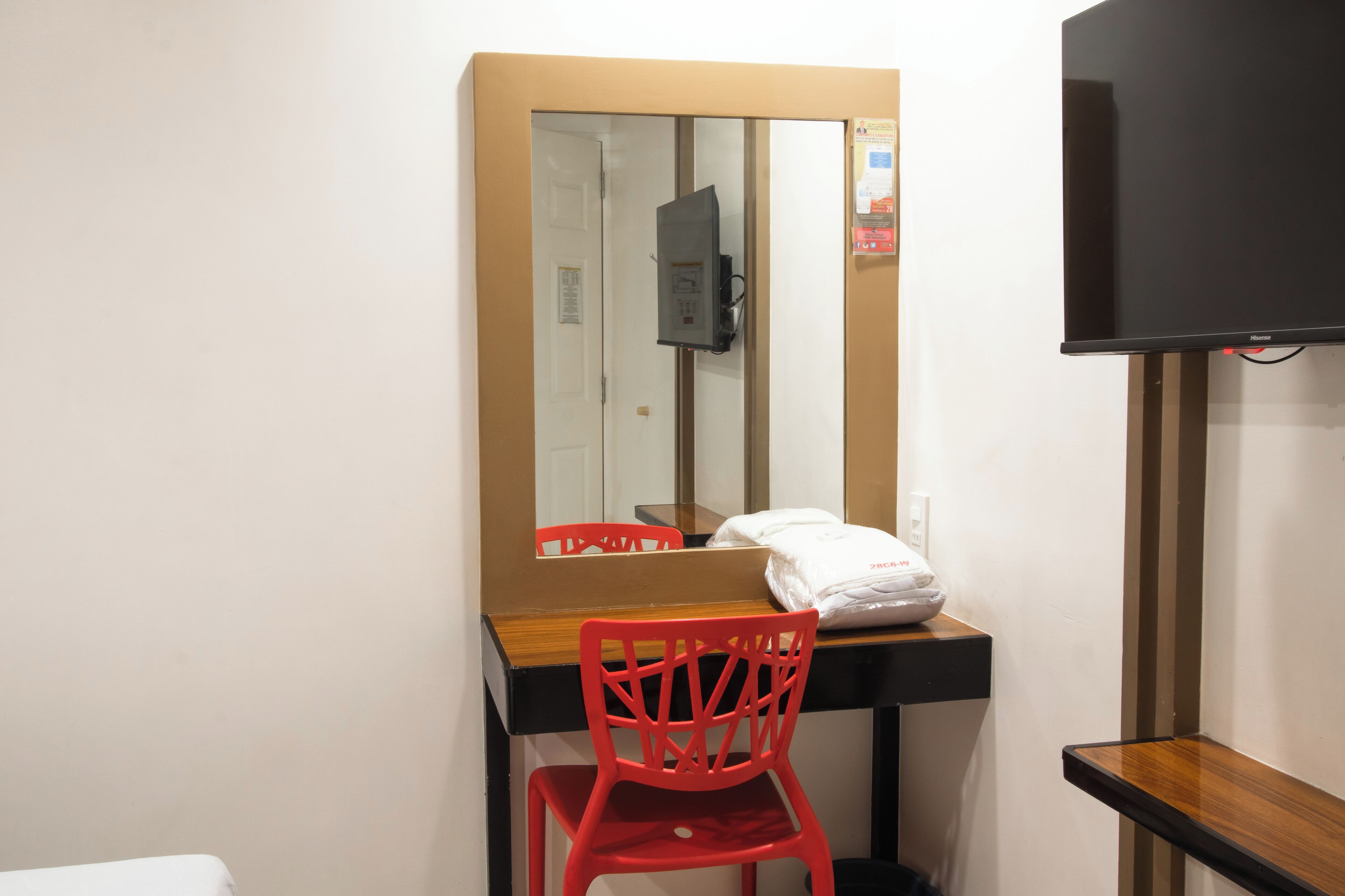 Een kleine kamer met een houten bureau, een rode stoel, een spiegel en een televisie.