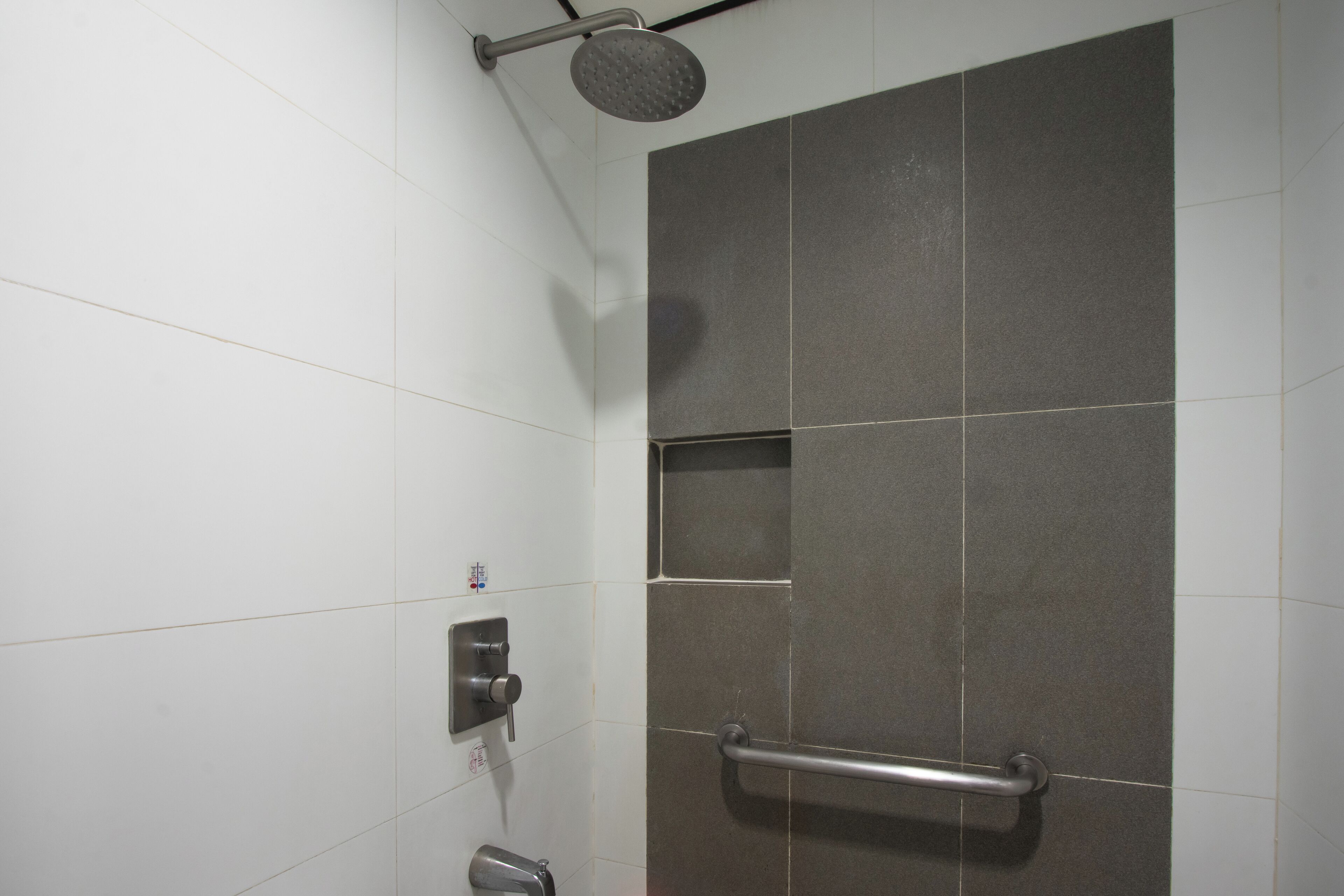 Un área de ducha con cabezal de ducha de mano, barra de apoyo y panel de control en la pared.