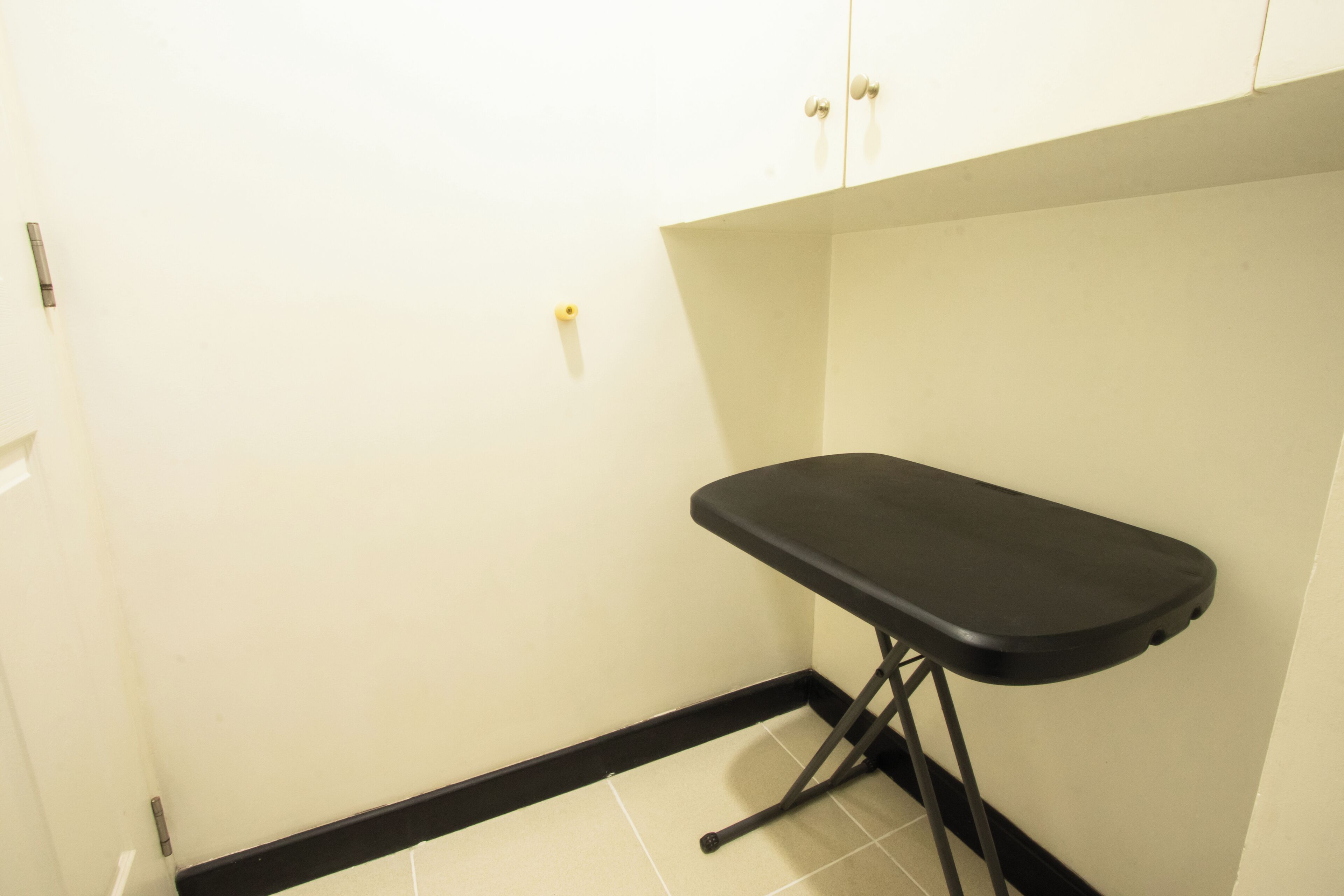 A corner of a room with a black ironing board against a white wall, a door, and a tiled floor.