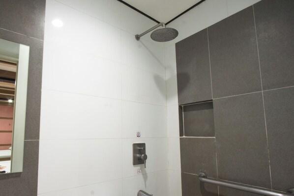 Una ducha con cabezal de ducha manual, panel de control y baranda.