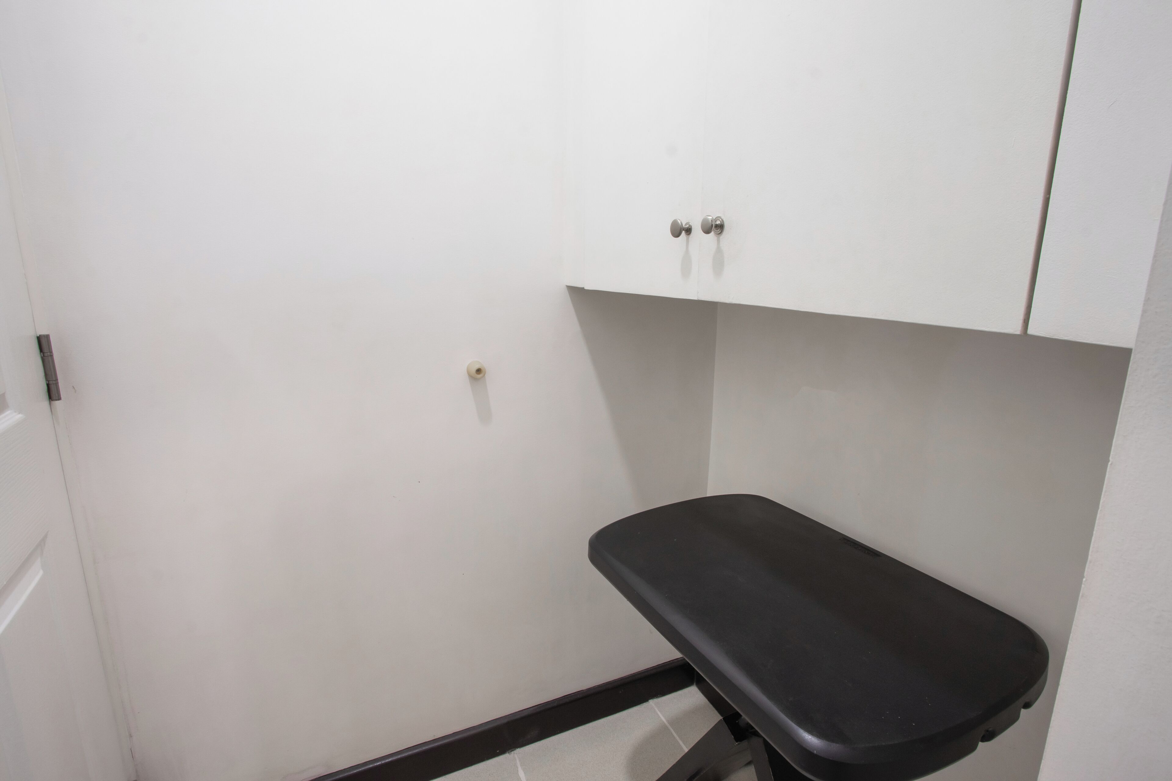 Pequeña habitación cerrada con un banco negro, paredes blancas y una puerta blanca.