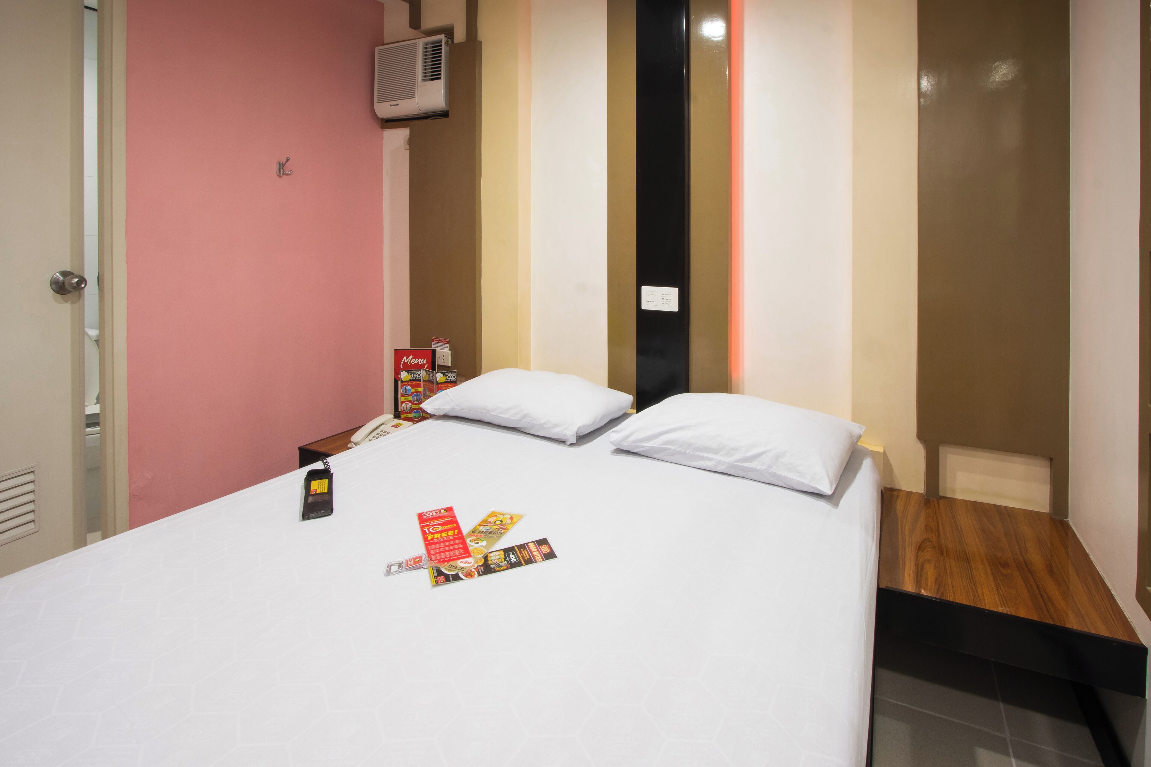 A hotel room with a bed, pillows, a nightstand, a phone, and a menu stand.