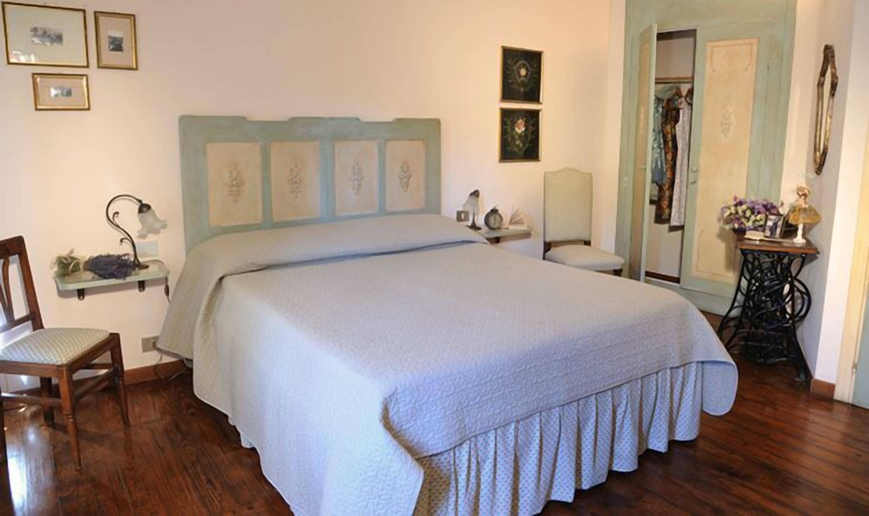 Een slaapkamer met een groot bed, een stoel, een nachtkastje en een naaimachine.