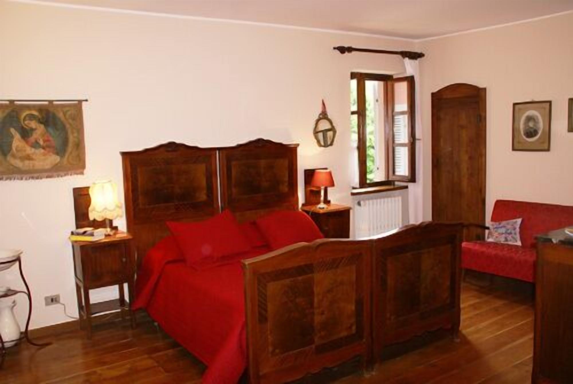 A bedroom with a wooden bed, a red sofa, a window with curtains, and a painting on the wall.