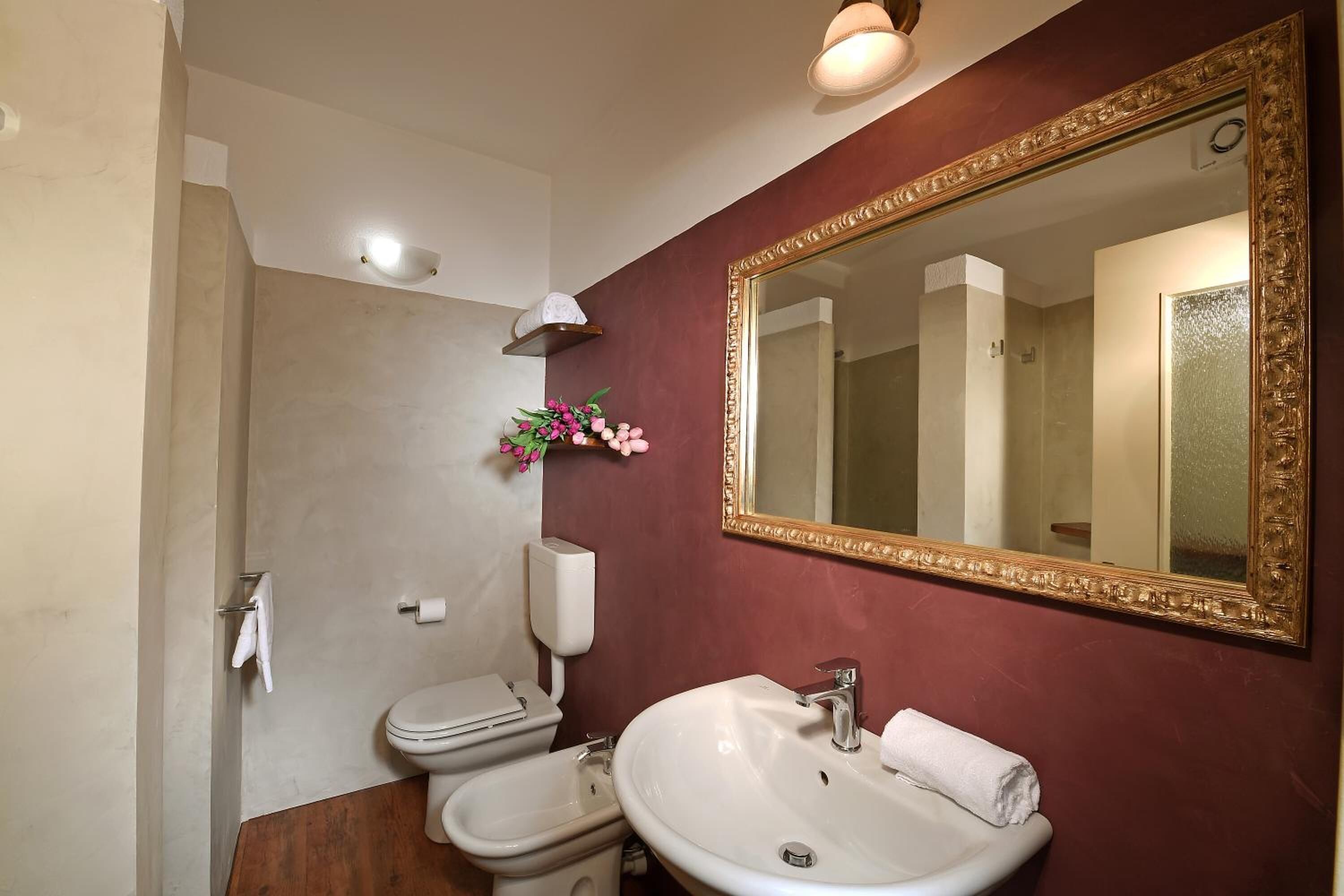 A bathroom with a toilet, bidet, and sink, a large mirror, and a wall-mounted light fixture.