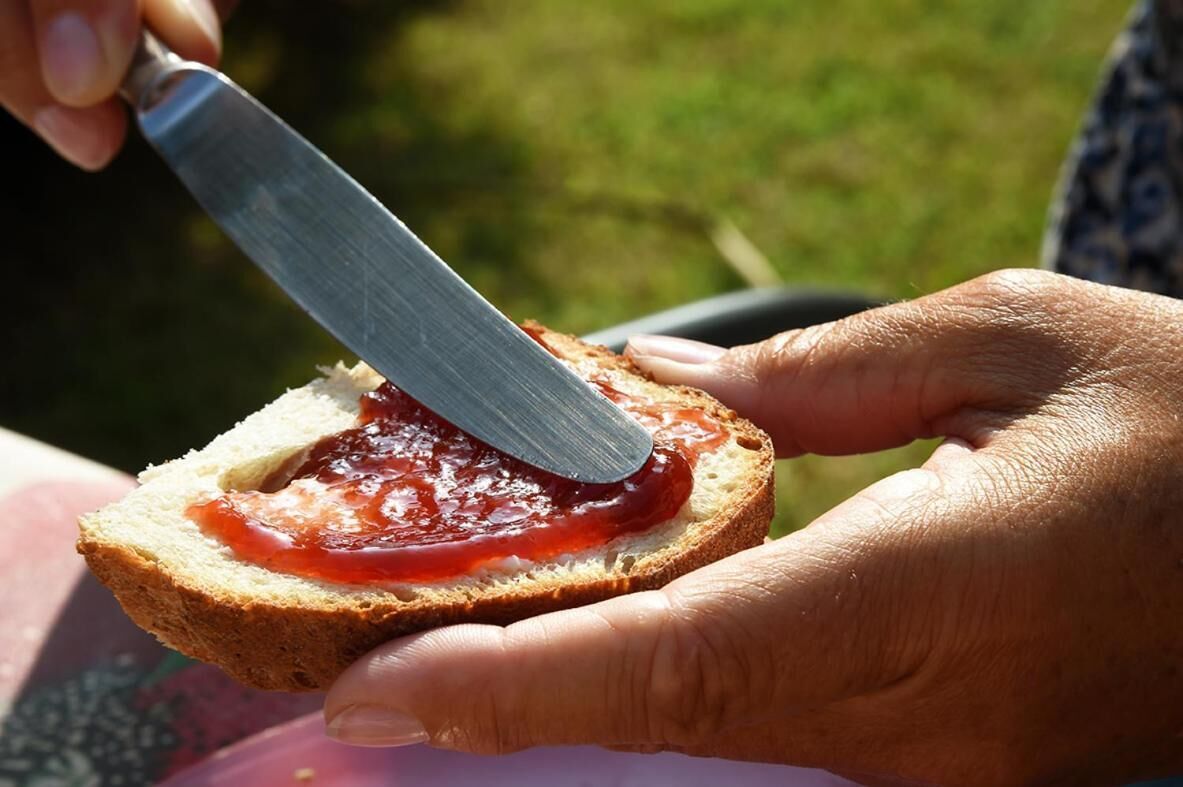A hand holding a slice of bread with jam spread on it.