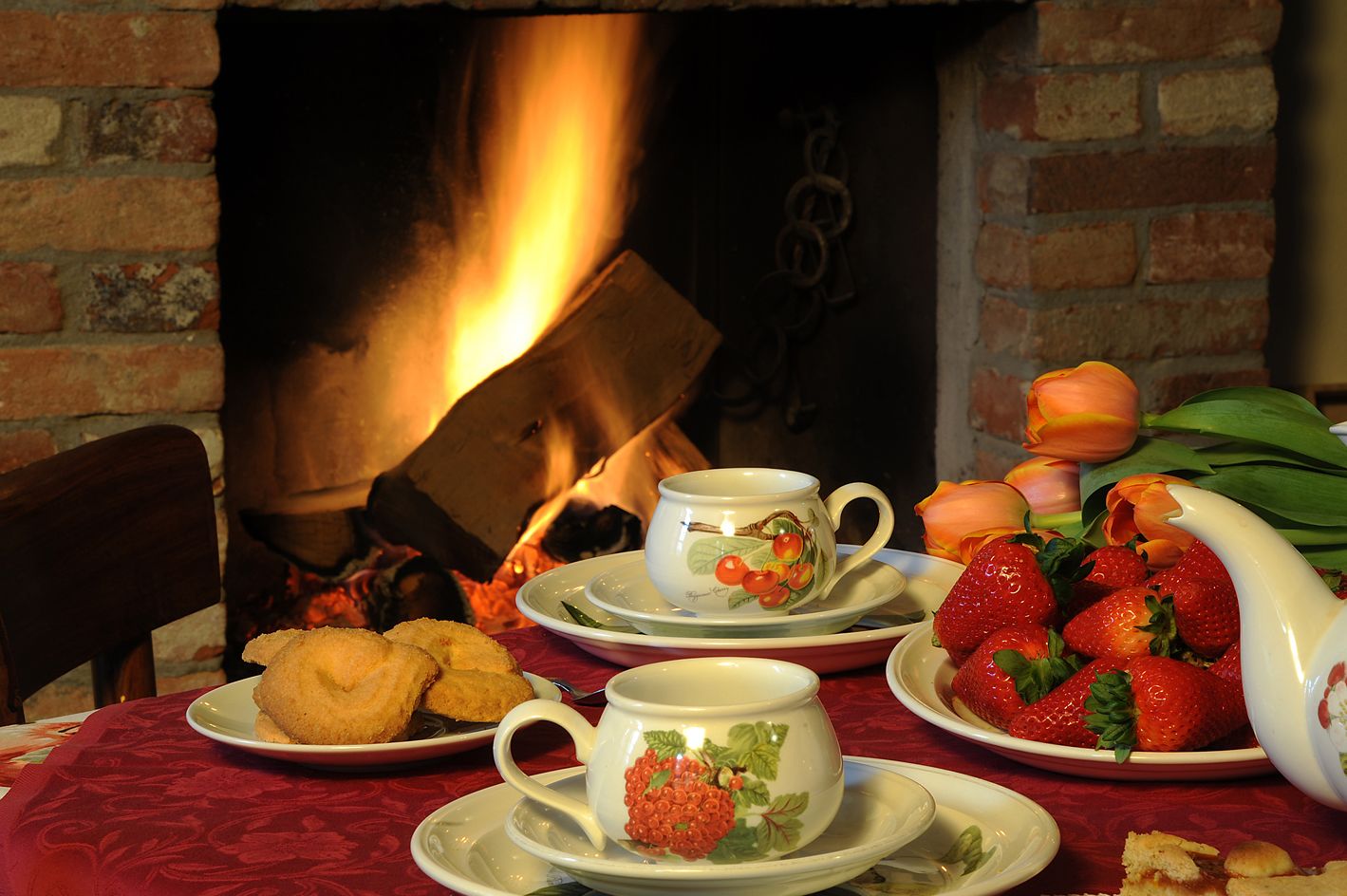 A table set with teacups, strawberries, cookies, and a vase of tulips.