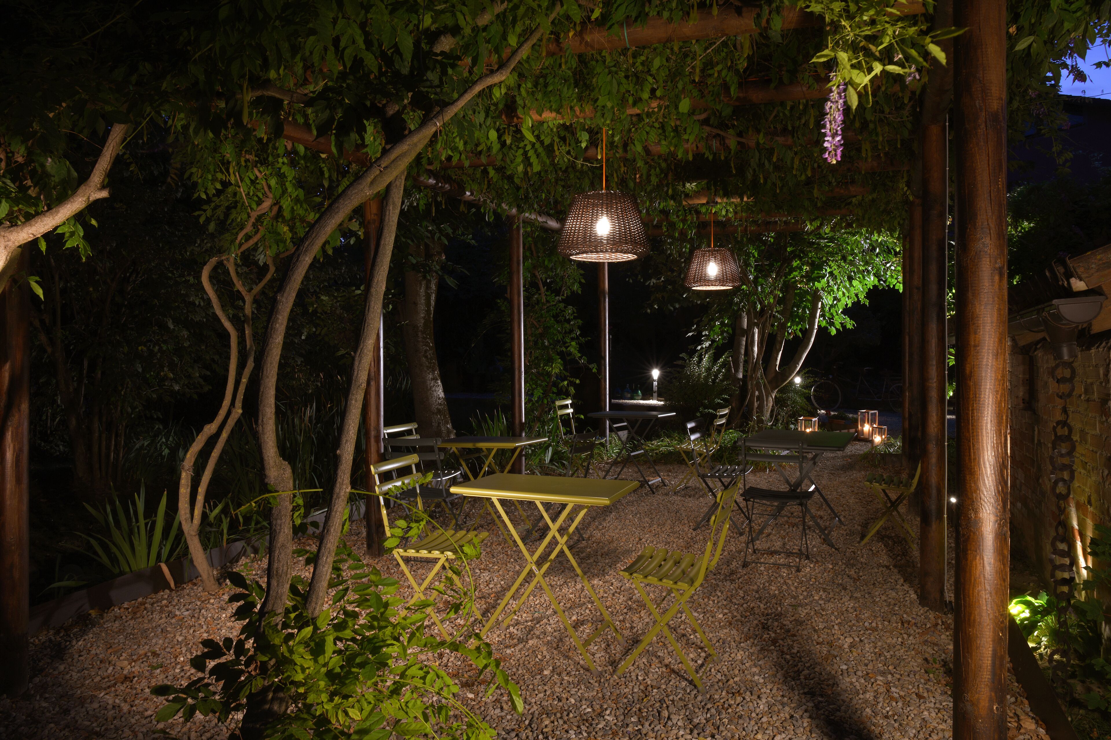 Un espacio al aire libre con mesas y sillas, rodeado de árboles y plantas.