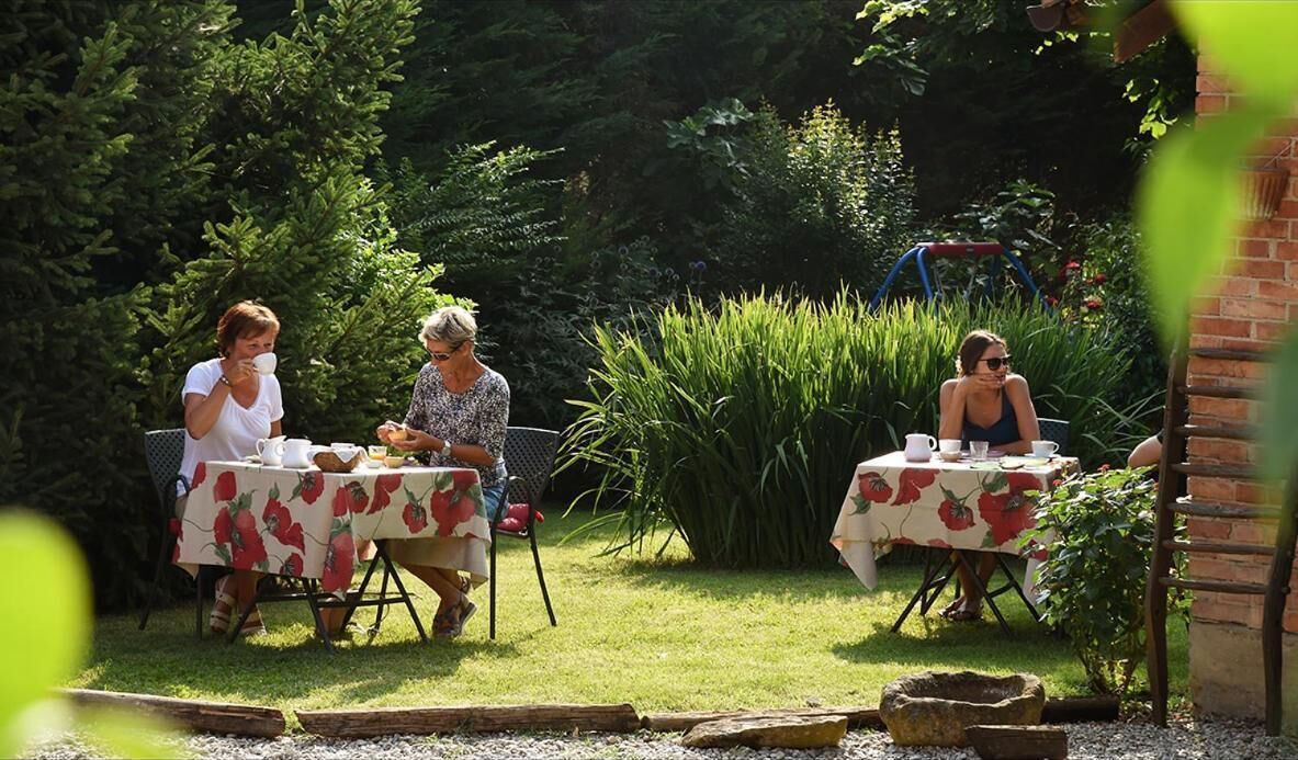 Three people seated at tables outdoors with a garden setting.