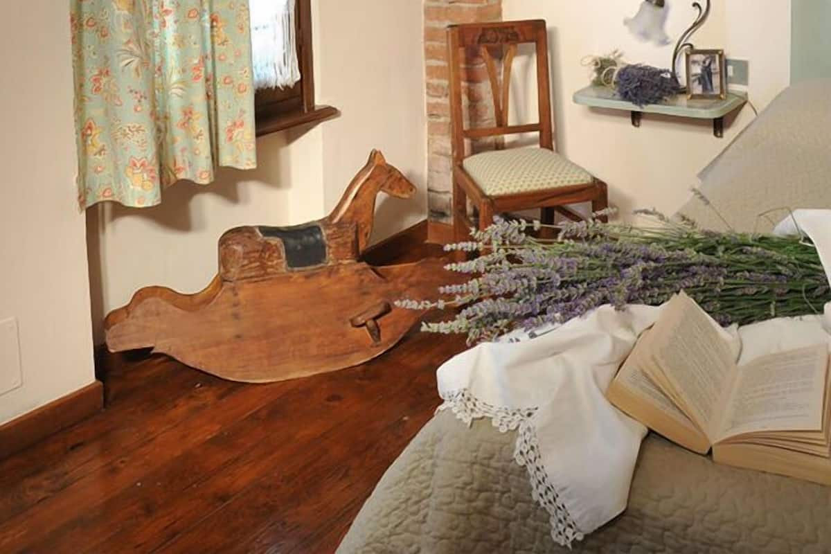 Une pièce chaleureuse avec une arche en briques, un cheval à bascule en bois, une chaise, un lit recouvert d’une courtepointe et une fenêtre ornée de rideaux à motifs floraux.