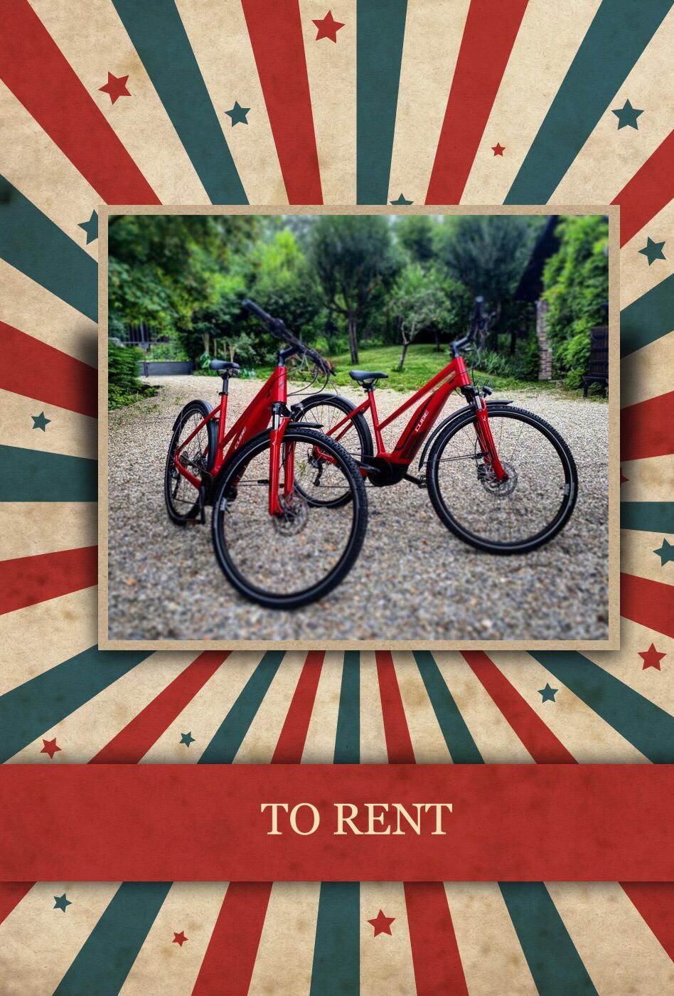 A red bicycle with a black seat and handlebars, parked on a gravel path in a park with trees and a bench in the background.