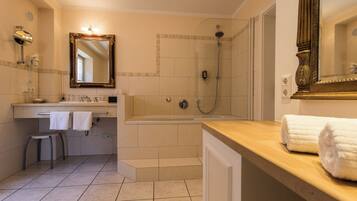 A bathroom with a bathtub, shower, vanity with a mirror, and a stool.