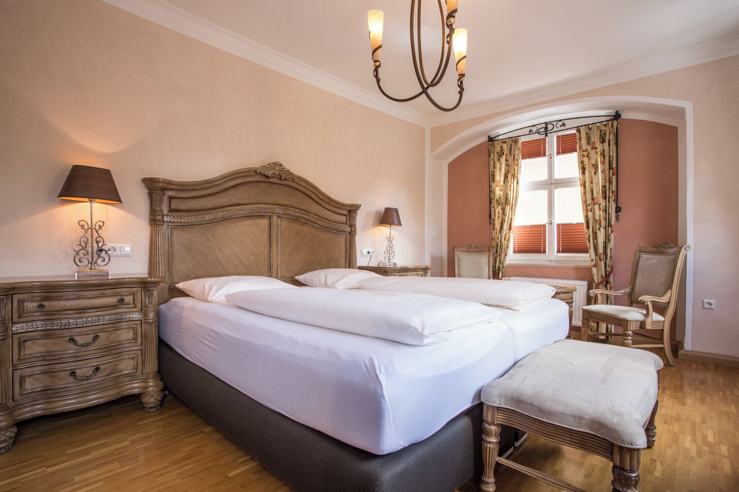 Un dormitorio con dos camas, un candelabro, una ventana con cortinas y una silla.