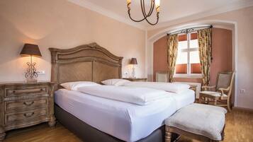 A bedroom with two beds, a chandelier, a window with curtains, and a chair.