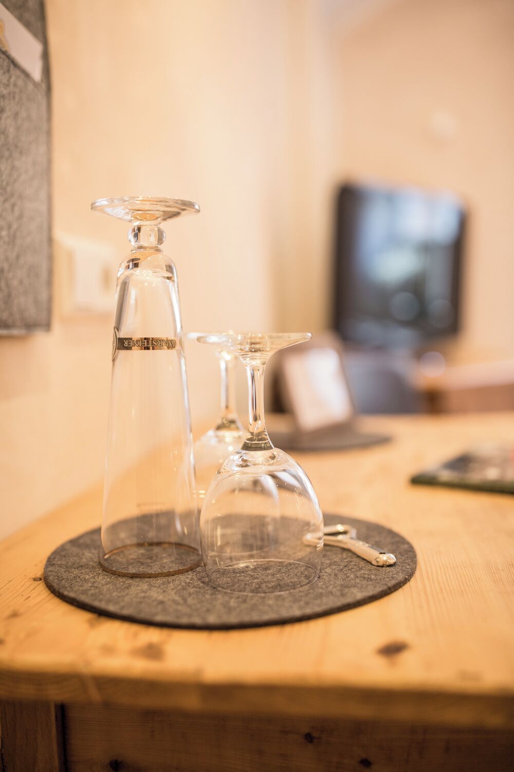 Two wine glasses on a wooden table with a television in the background.