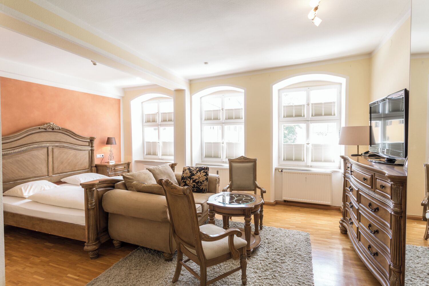 A bedroom with a bed, a sofa, a chair, a small table, a dresser, and a TV.