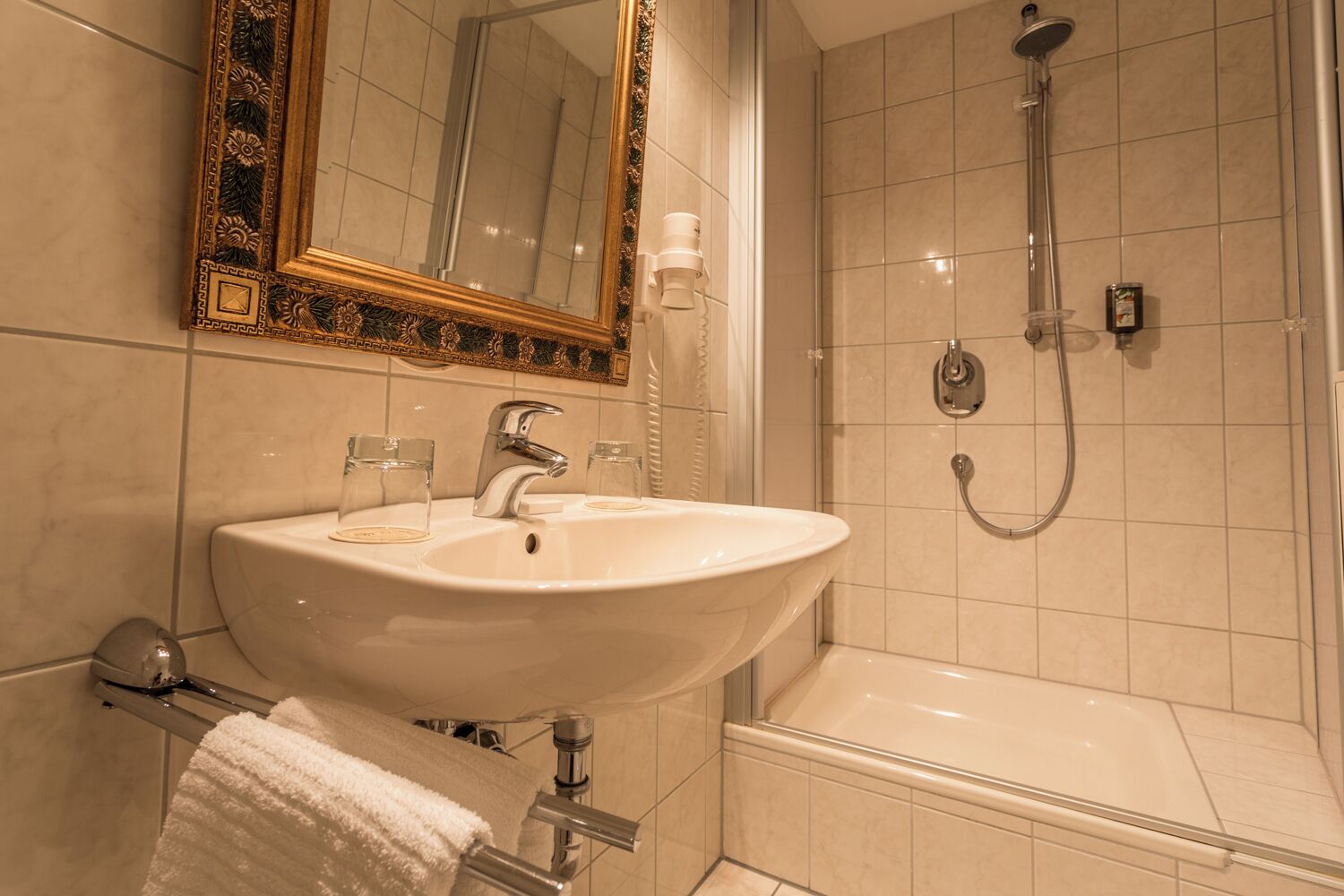 A bathroom with a sink, mirror, shower, and towel rack.