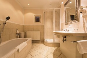 Baño con bañera, cabina de ducha, inodoro, radiador, lavabo, espejo y secador de pelo.
