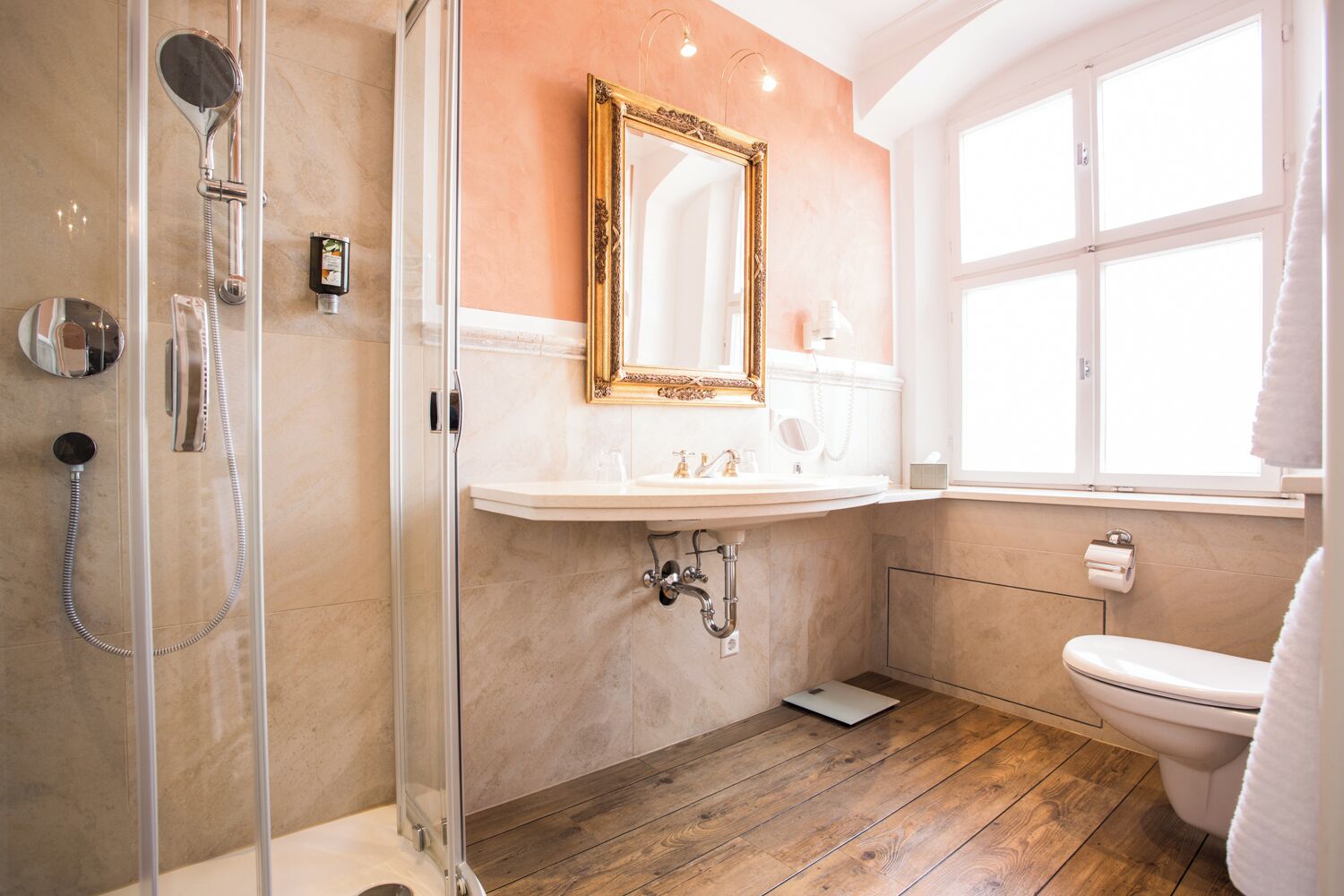 Une salle de bain avec une douche à parois de verre, un lavabo blanc, des toilettes et un grand miroir avec un cadre doré.