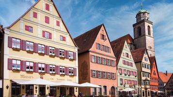 A traditional European street with colorful buildings, a prominent clock tower, and outdoor seating at a café.