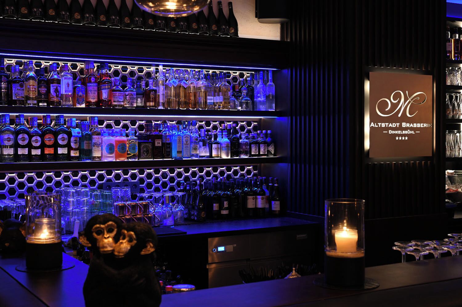 Un bar con varias estanterías llenas de botellas de licor, un cartel con un monograma y una figura decorativa de un mono.