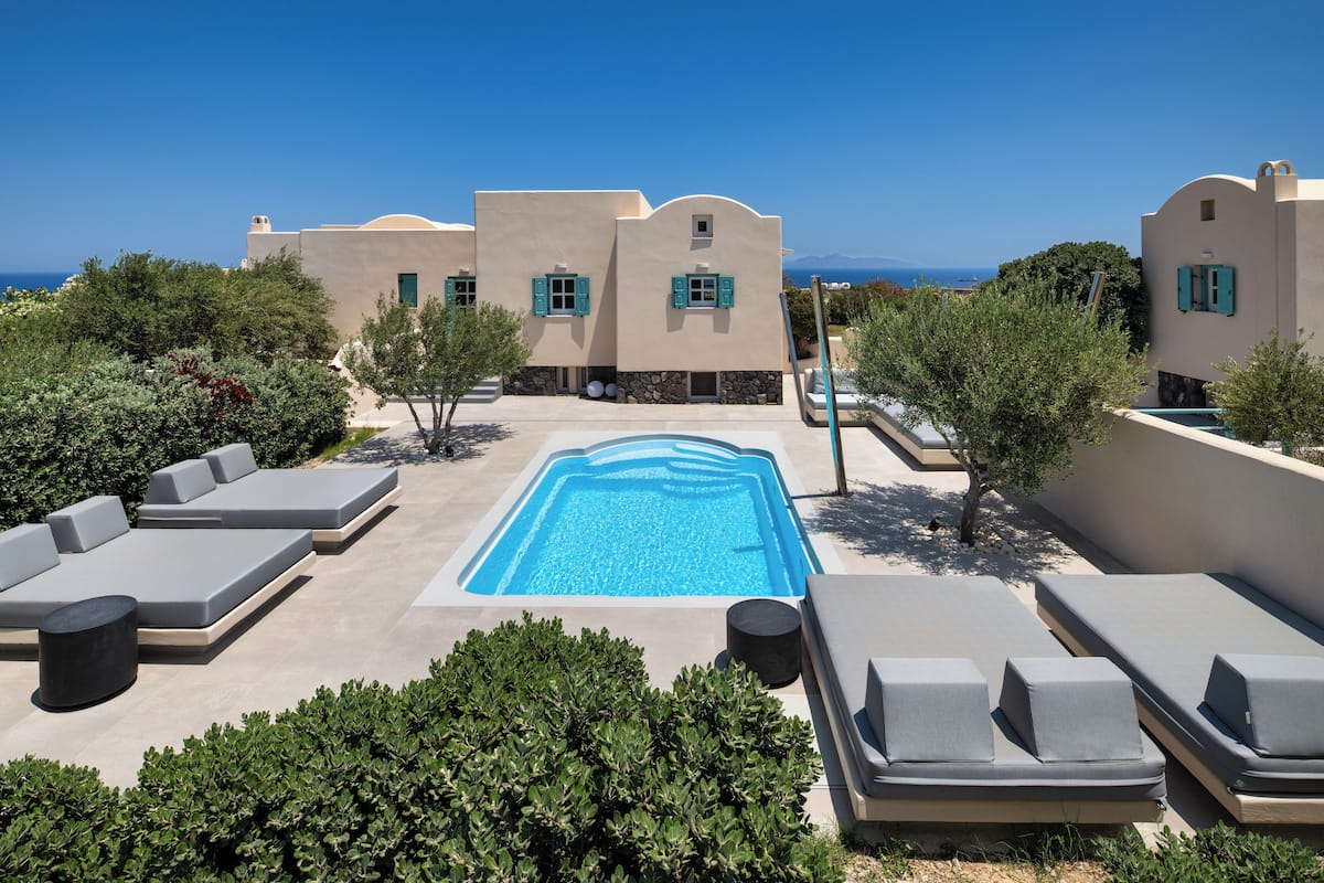 A rooftop pool area with lounge chairs and a swimming pool, surrounded by greenery and a view of the sea.