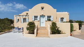 A Mediterranean-style building with a curved facade, a central entrance with steps, and a terrace with outdoor seating. - Sienna Eco Resort (Santorini)
