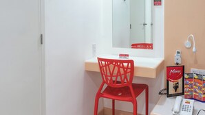 Ein Badezimmer mit einem weißen Waschbecken, einem roten Stuhl, einem Spiegel, einem weißen Telefon und einem Poster an der Wand.