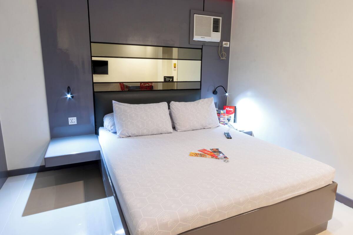 A modern bedroom with a large bed, a bedside table with a lamp, and a mirror above the bed.