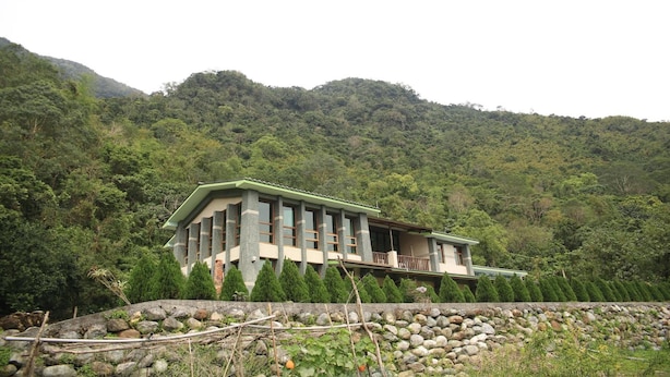 Um edifício moderno com varanda, rodeado por um muro de pedra e vegetação exuberante.