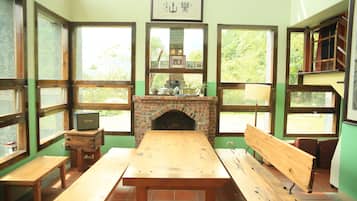 A room with a brick fireplace, wooden benches, and large windows with wooden frames.