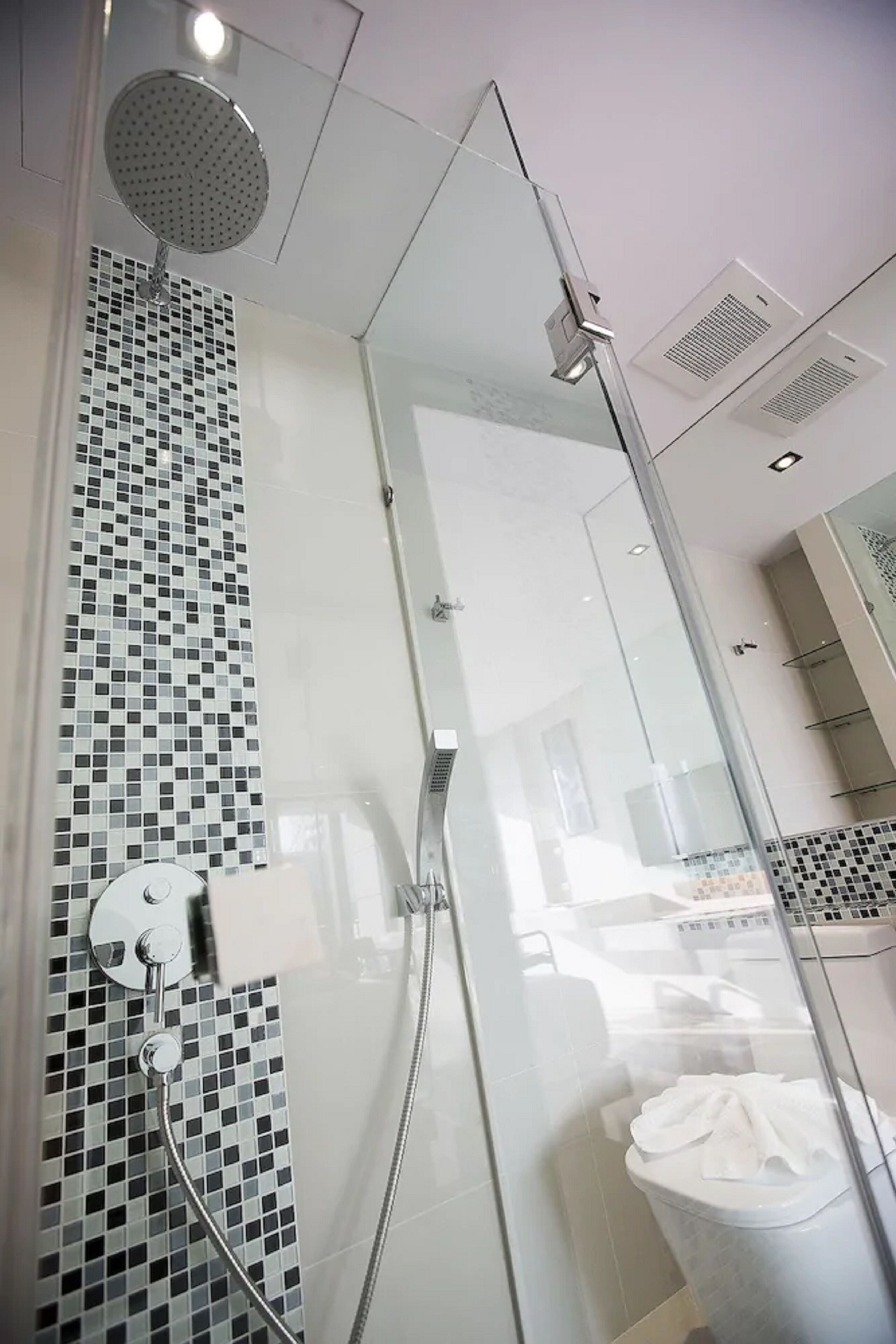 A modern bathroom with a glass-enclosed shower, a tiled wall, and a toilet with a towel.