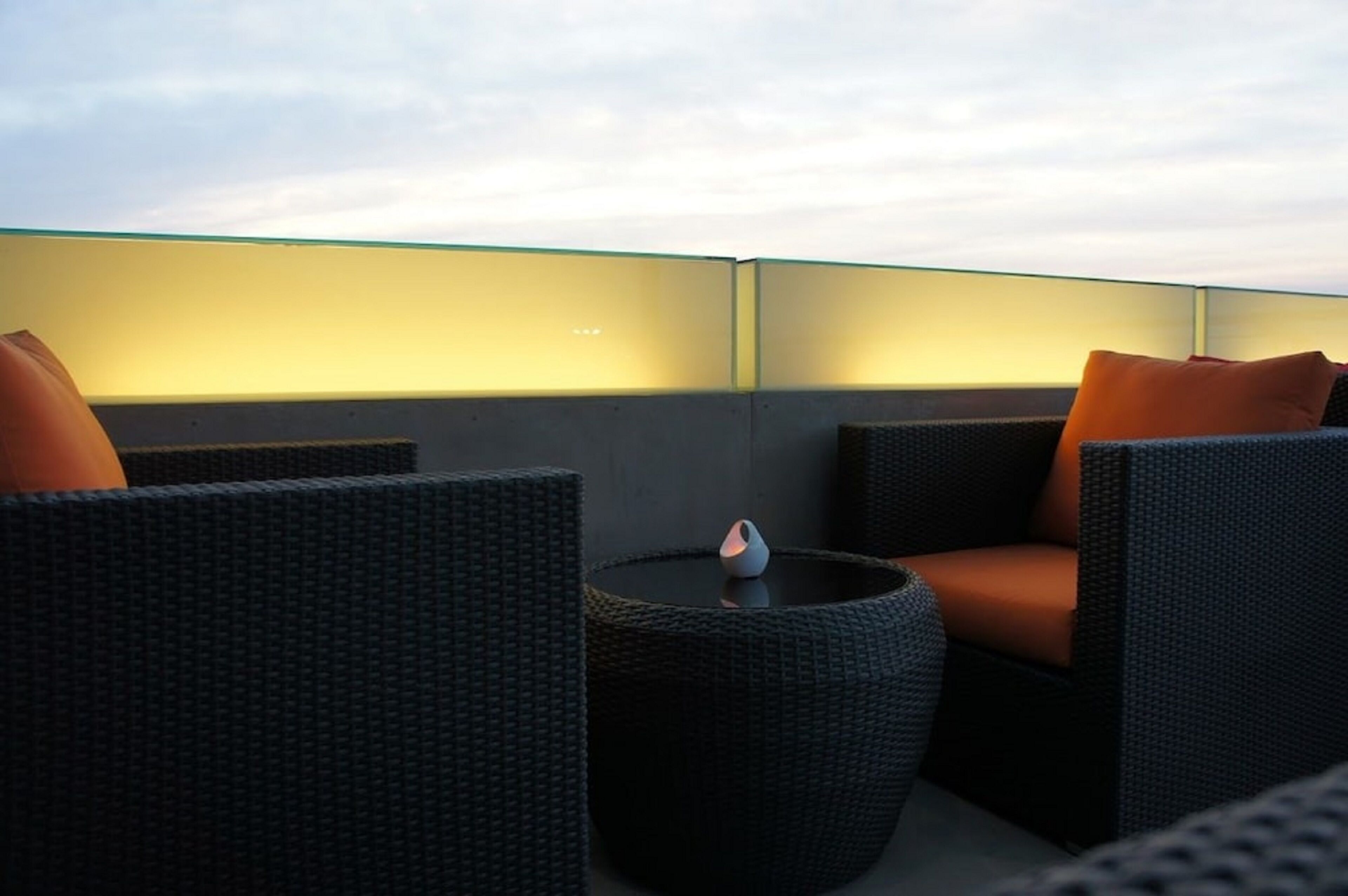 A rooftop seating area with wicker furniture and a glass partition.