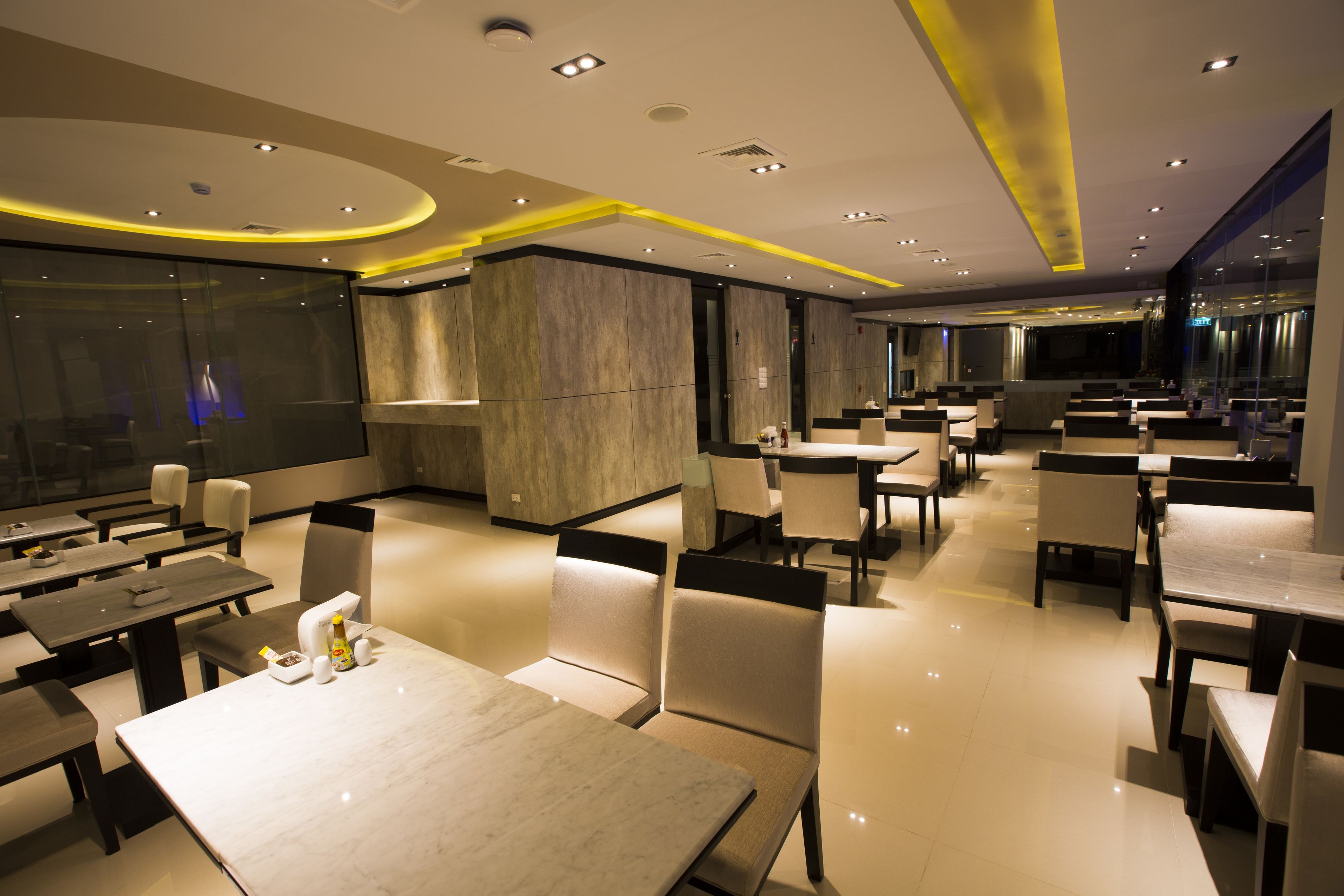 A modern restaurant with multiple dining areas, including booths and tables, and a large glass wall providing a view of the cityscape.