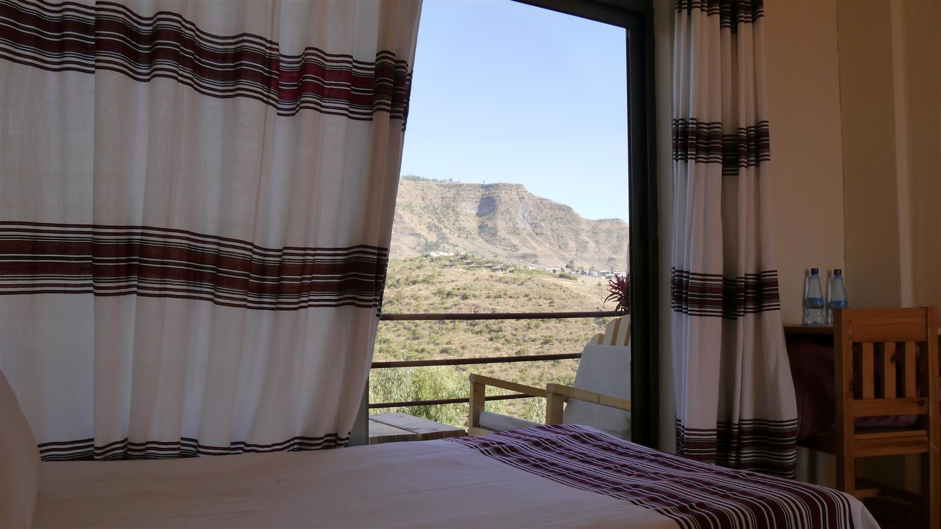 Une chambre avec un lit, une vue sur un paysage montagneux et un balcon avec une chaise.