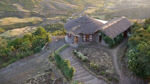 A thatched-roof house with a stone foundation, surrounded by terraced fields and a valley.