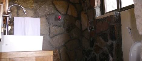 Un baño con pared de piedra, tocador de madera, lavabo blanco y ventana.