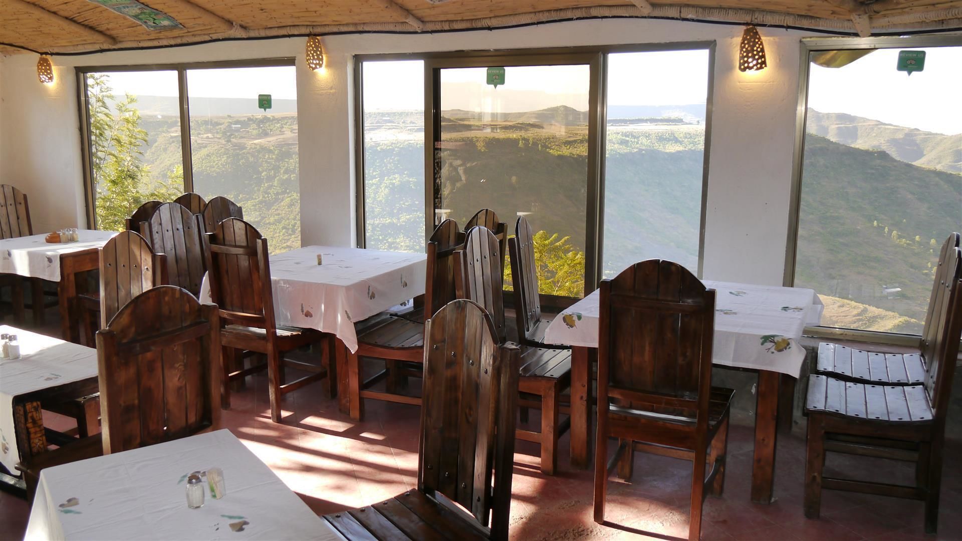 Un espace repas avec des tables et des chaises en bois, de grandes fenêtres offrant une vue sur la campagne.