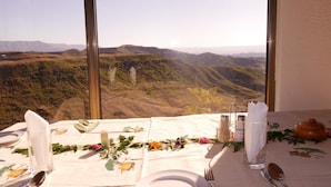 A table set for dining with a view of a mountainous landscape through large windows.