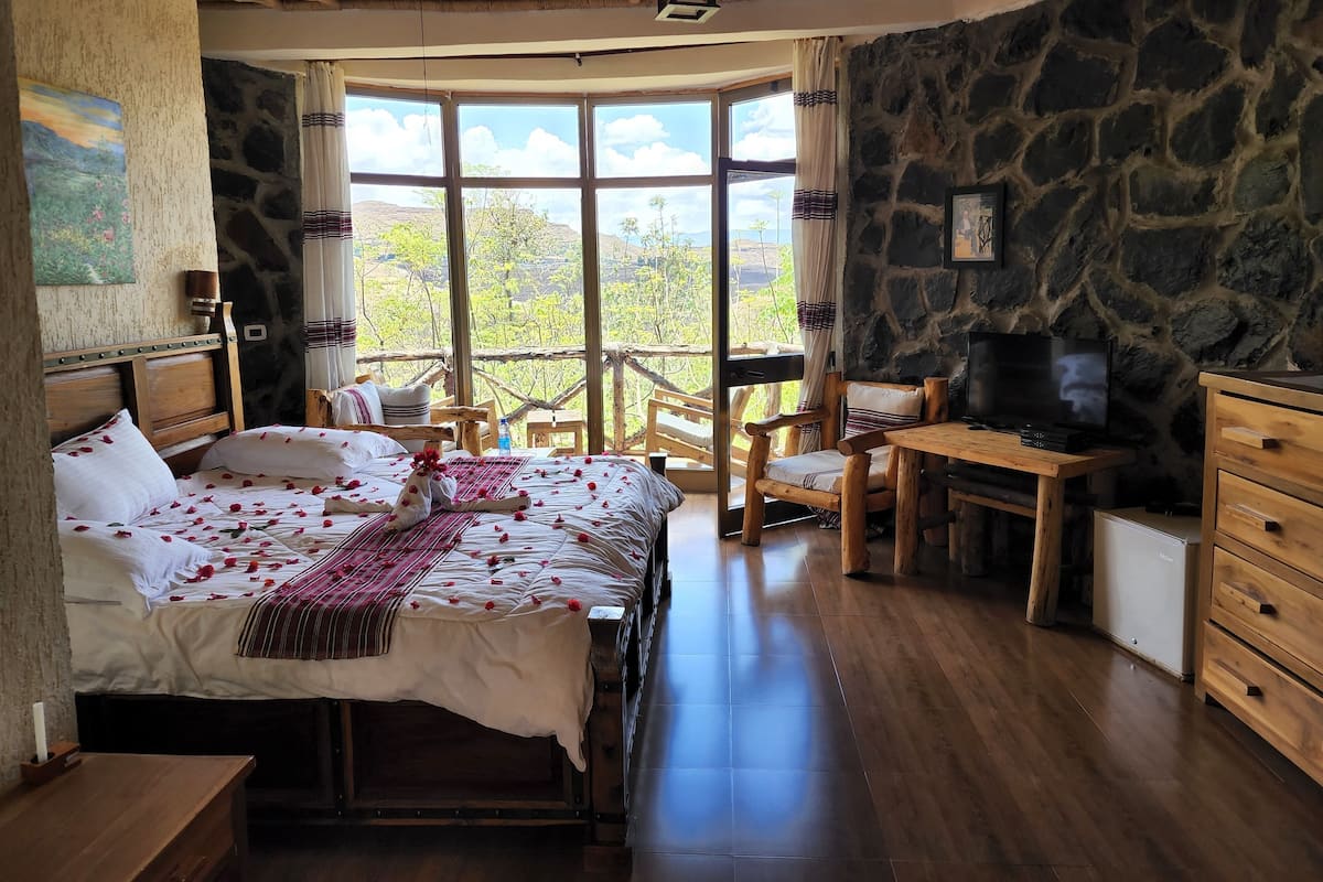Une chambre avec un lit, un bureau, une télévision et un mur en pierre.