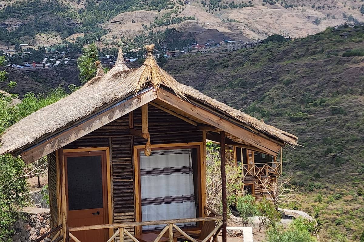 Un chalet rustique en bois, doté d’un toit de chaume, d’un balcon et offrant une vue sur un paysage montagneux.