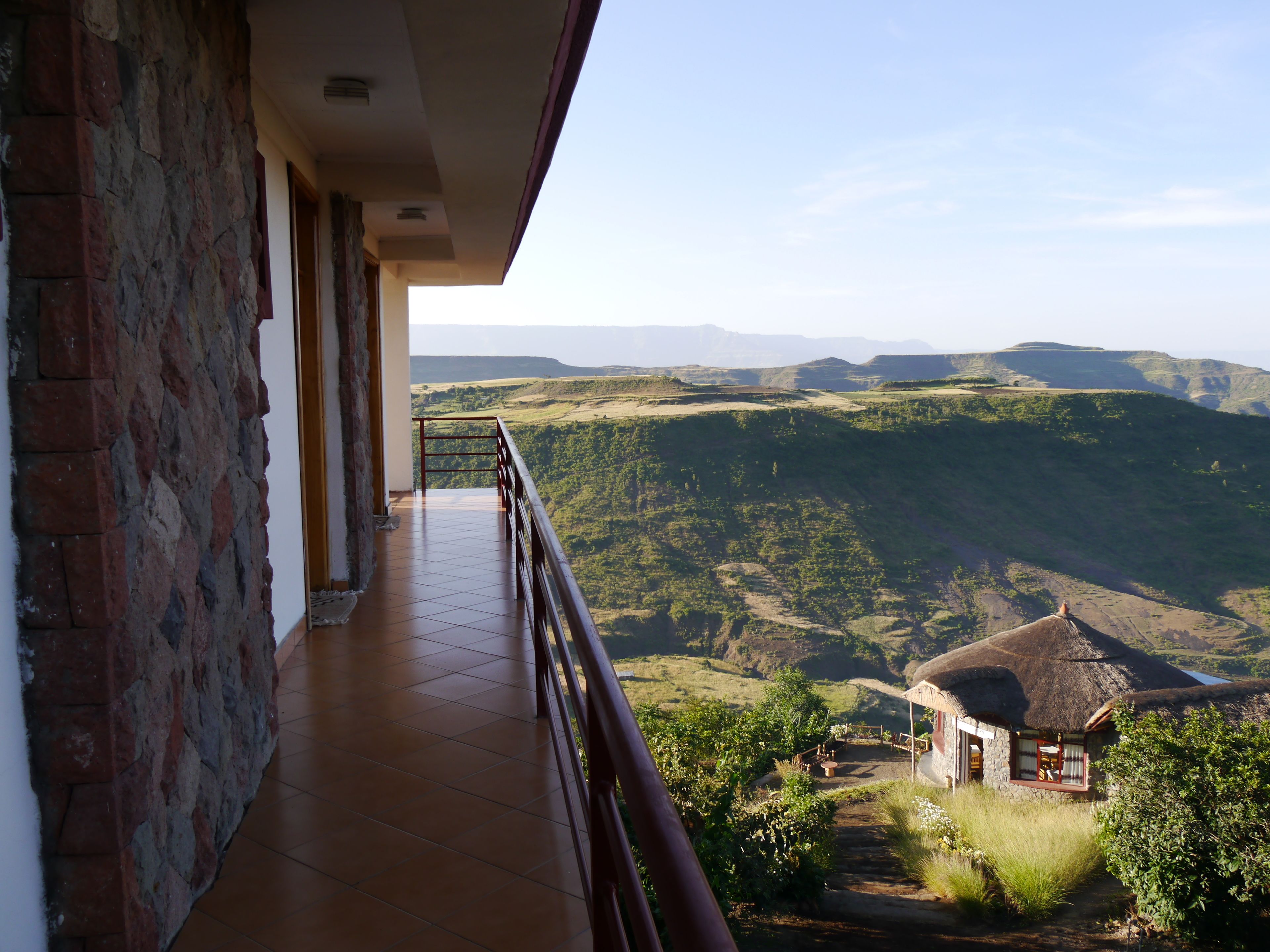 Un balcón con vistas a un valle y un edificio con techo de paja.