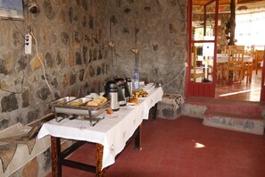 A buffet setup with a stone wall, a table with a white tablecloth, and various food items and beverages.