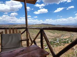 A wooden deck with a chair and table overlooking a valley with scattered buildings.