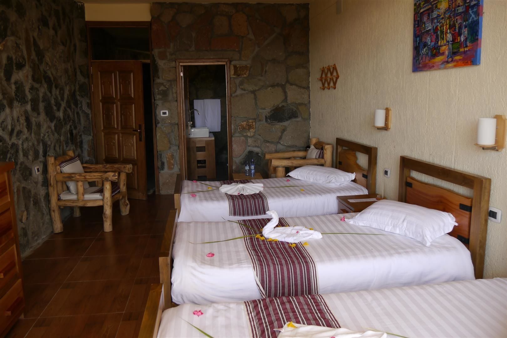 Une chambre d’hôtel avec trois lits, des meubles en bois, des murs en pierre et un tableau accroché au mur.